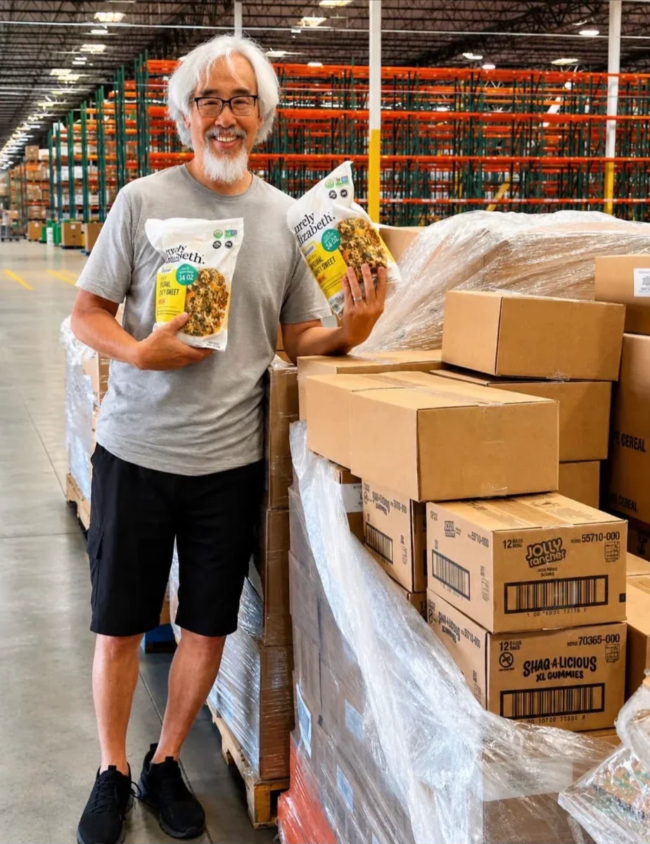 Mark Chow standing beside pallets of donated goods in a warehouse